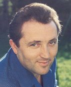 Phtographie von Fritz Wunderlich im blauen Hemd, nur Kopf und Schultern zu sehen. Im Hintergrund ein Garten.