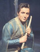 Photographie von Fritz Wunderlich in blau-goldenem Kostüm auf einer Bühne, eine Holzflöte haltend.